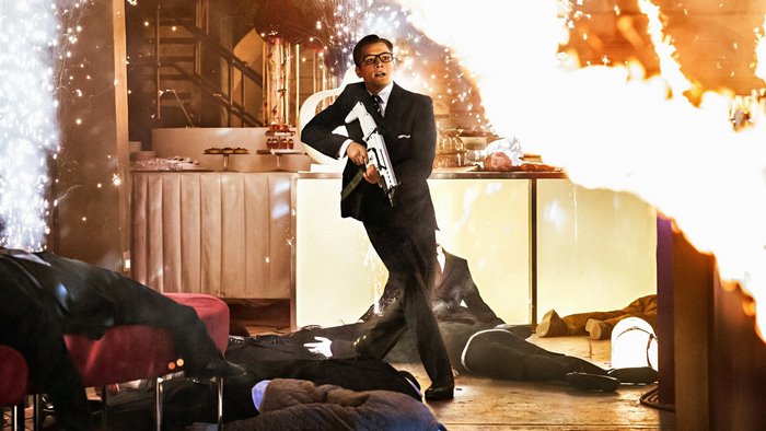 Taron Egerton in a suit with a gun