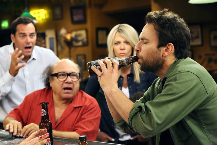 Four people at a bar, one drinking from a bottle
