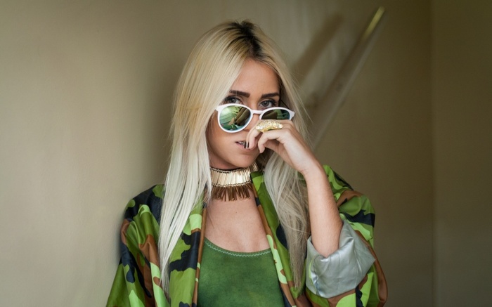 Woman with blonde hair wearing sunglasses and camouflage jacket