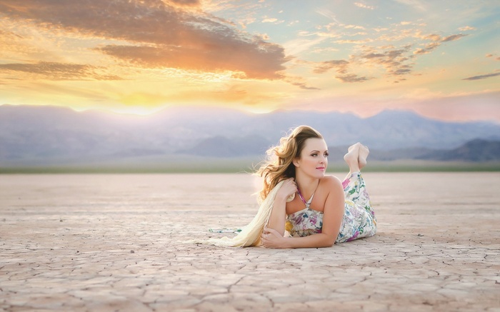 Woman lying on cracked earth at sunset