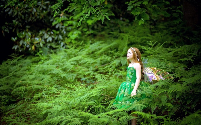 Girl in green dress with fairy wings in a fern forest