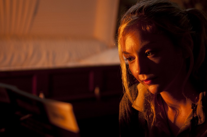 Emily Kinney in a dimly lit room with a coffin