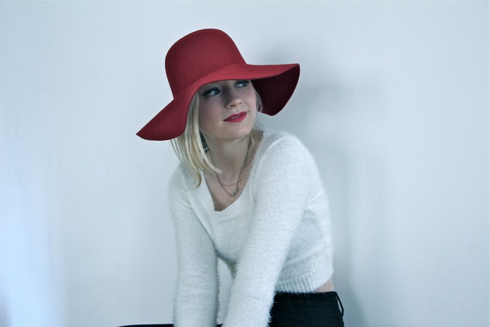 Emily Kinney wearing a red hat and white sweater