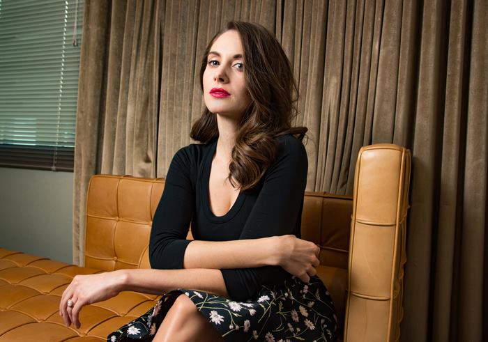 Alison Brie sitting on a couch