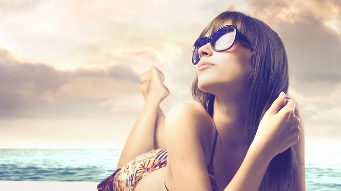 Woman in sunglasses sunbathing by the ocean