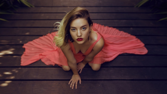 Woman in a pink dress kneeling on a wooden deck