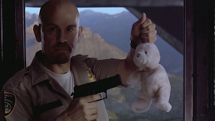 John Malkovich holding a teddy bear and a gun