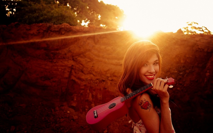 Woman holding a pink ukulele at sunset
