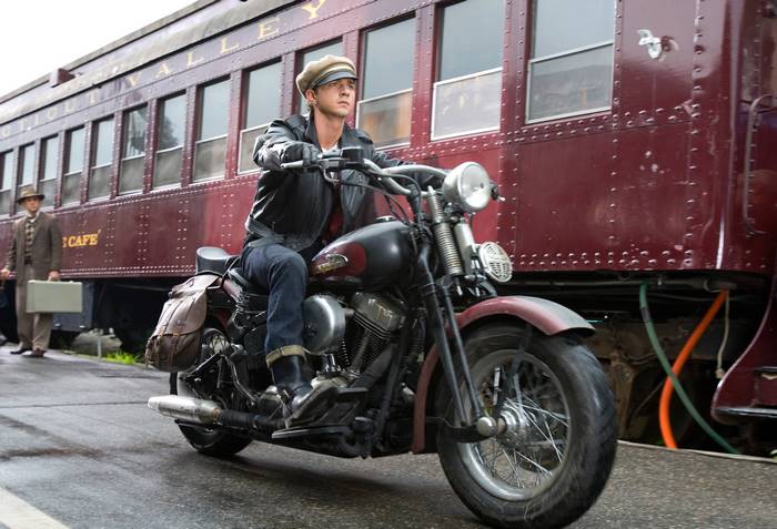 Shia LaBeouf riding a motorcycle near a train