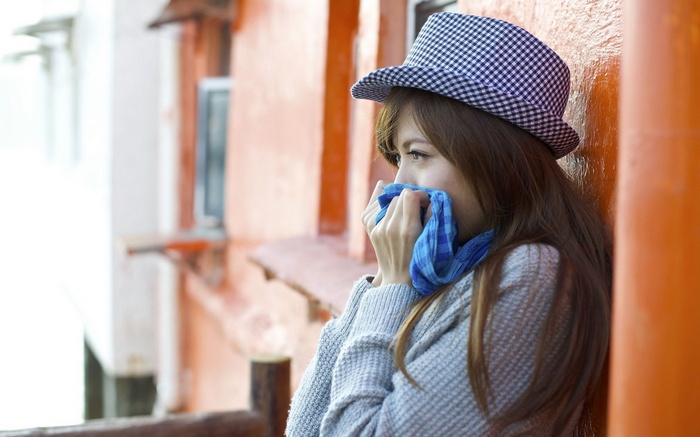 Woman in hat covering mouth with blue cloth
