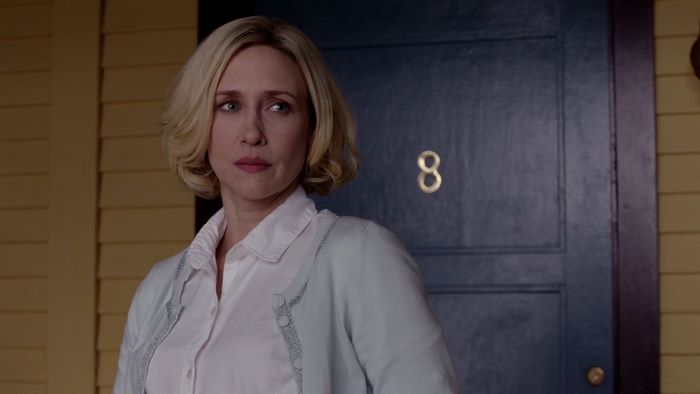 Vera Farmiga standing by a blue door with number 8