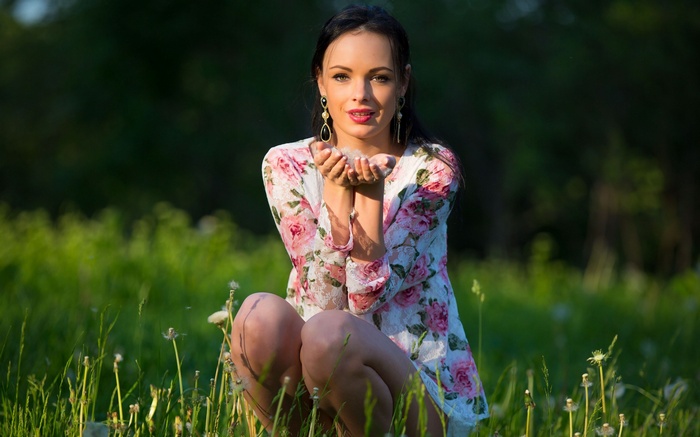 Woman in floral dress blowing dandelion seeds in a field