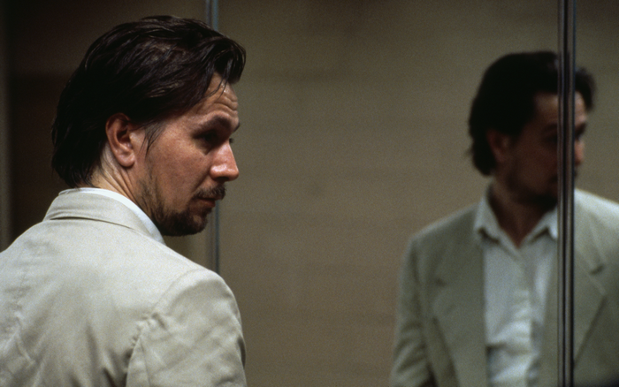 Gary Oldman in a suit looking in a mirror
