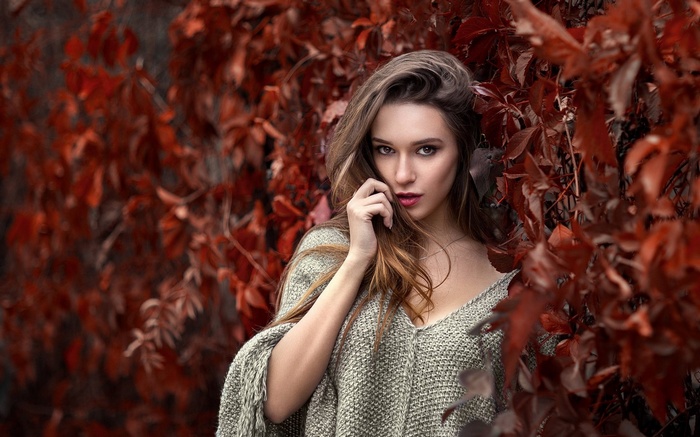 Woman in a knitted poncho among red leaves