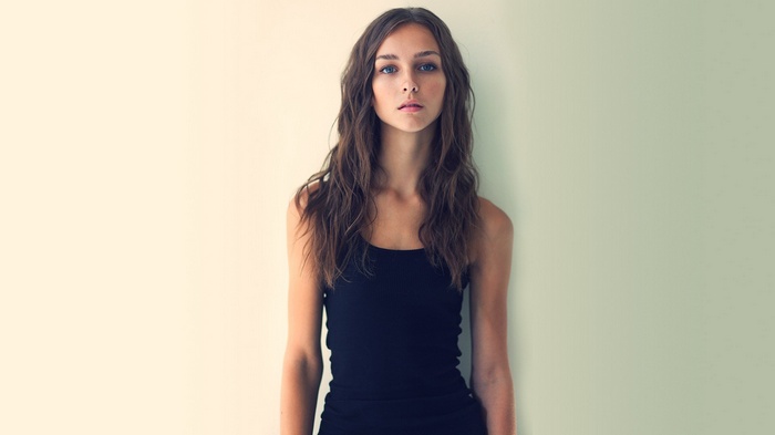 Young woman in black tank top against a wall