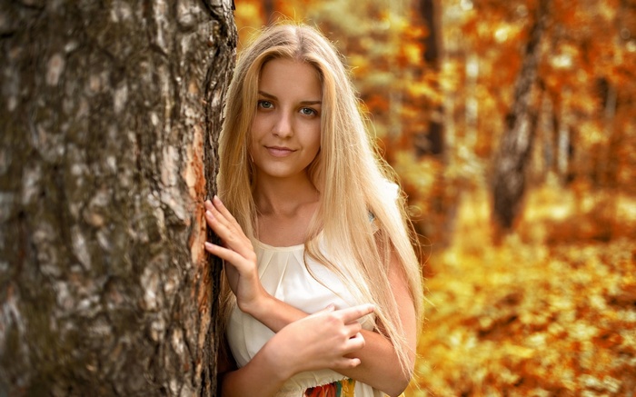 Young woman with blonde hair leaning against a tree