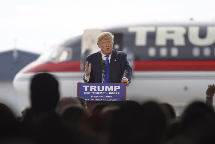 Donald Trump speaking at a podium with a plane behind him