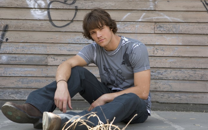 Jared Padalecki sitting in front of a wooden wall