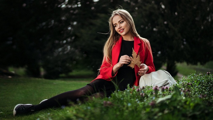 Woman in red coat holding a leaf in a park