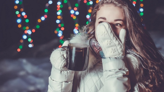 Woman holding a hot drink with Christmas lights