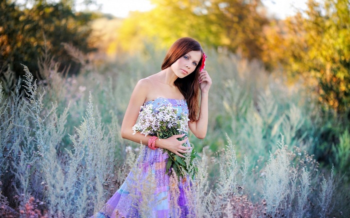 Woman in a floral dress holding flowers in a field