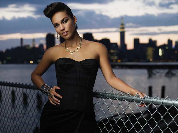 Alicia Keys posing by a fence with New York City skyline