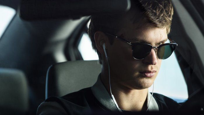 Ansel Elgort wearing sunglasses and earphones in a car