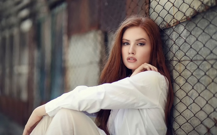 Woman with red hair sitting by a fence