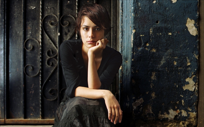 Shannyn Sossamon sitting by a weathered wall