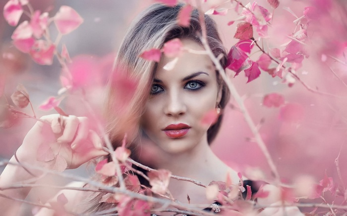 Woman with blue eyes and red lips behind pink leaves