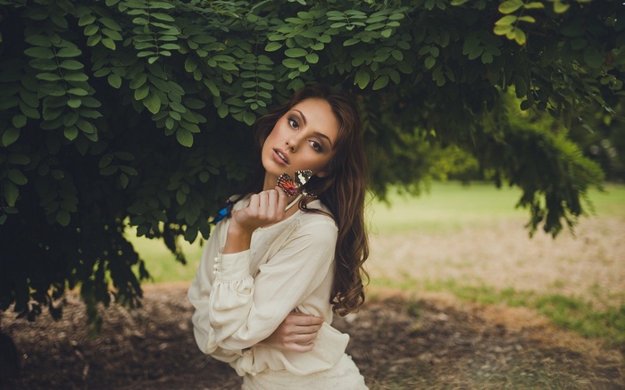 Woman holding a butterfly under a tree
