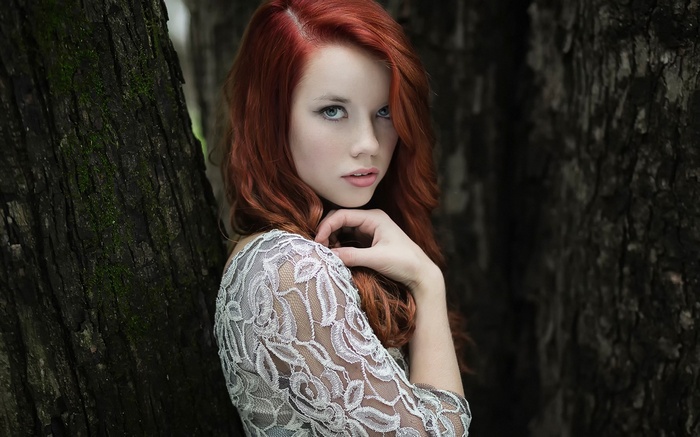 Woman with red hair in a lace dress near trees