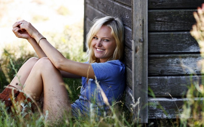 Malin Åkerman sitting by a wooden structure