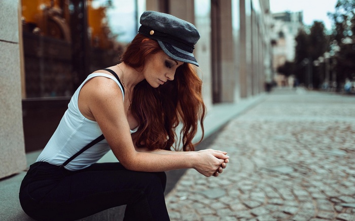 Woman with red hair wearing a cap and white tank top