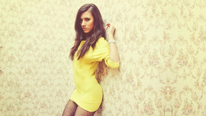 Woman in yellow dress leaning against floral wallpaper