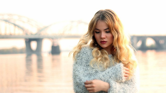 Young woman with blonde hair in a grey sweater by a bridge