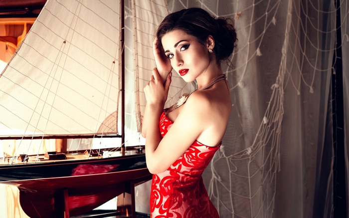 Woman in red dress posing by a model sailboat