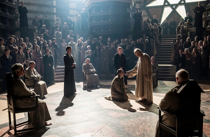 Jonathan Pryce in a large hall with many people