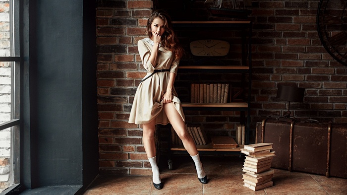Woman in dress posing in a room with brick wall