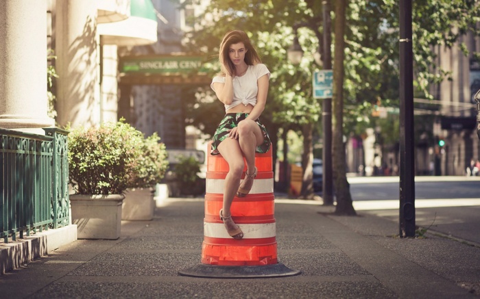 Woman sitting on a traffic barrel on a city street