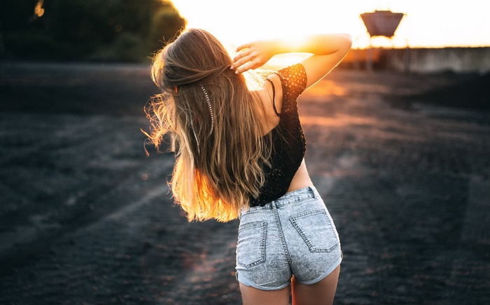 Woman in denim shorts and black top at sunset