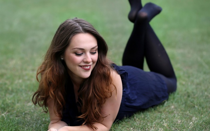 Woman lying on grass wearing a dark blue dress