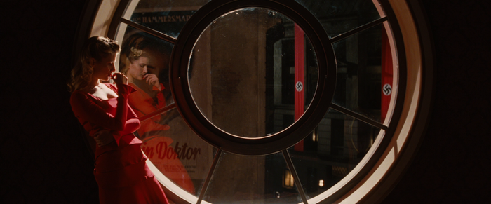 Mélanie Laurent in a red dress looking through a window