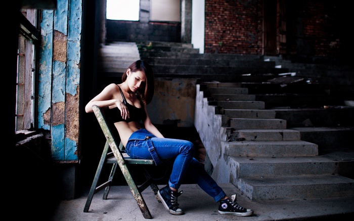 Woman in denim overalls sitting on a chair in an abandoned building