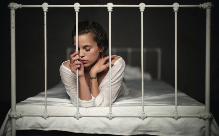 Woman lying on a bed behind bars