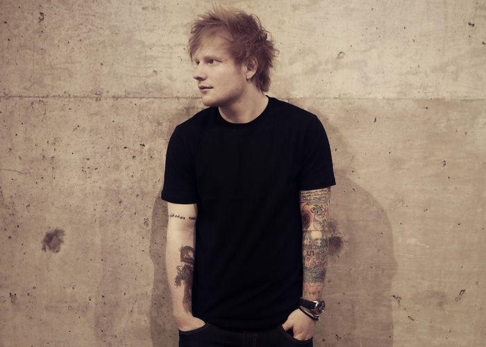 Ed Sheeran standing against a concrete wall