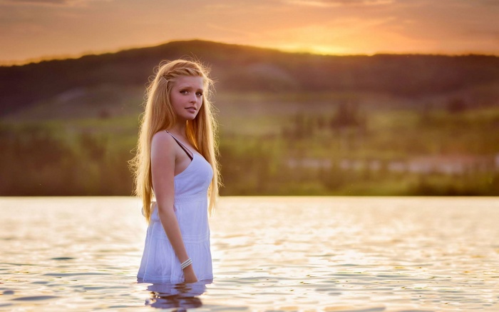 Young woman in white dress standing in water at sunset