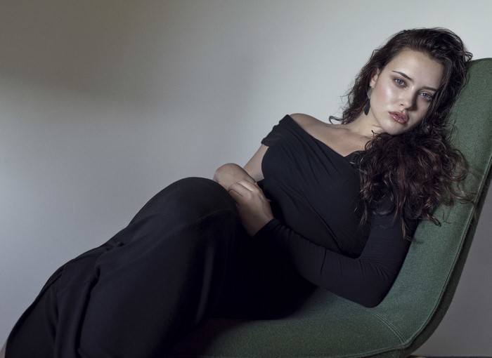 Katherine Langford in a black dress sitting in a chair