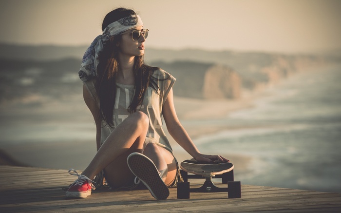 Woman with bandana and sunglasses sitting with skateboard