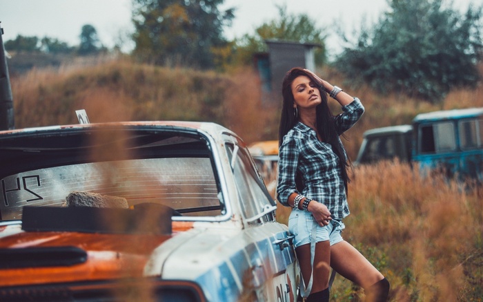 Woman leaning on a rusty car in a field